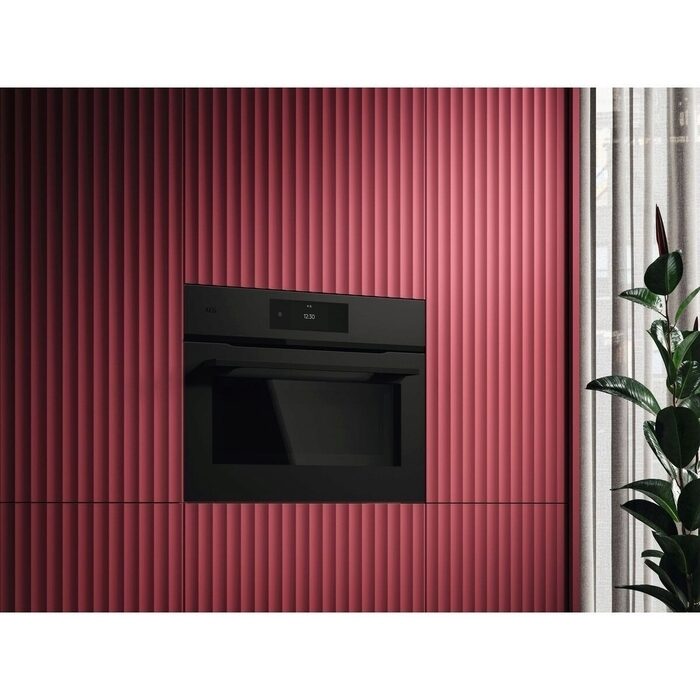 Black AEG Combi oven embedded in a red ribbed wall with a plant on the right.