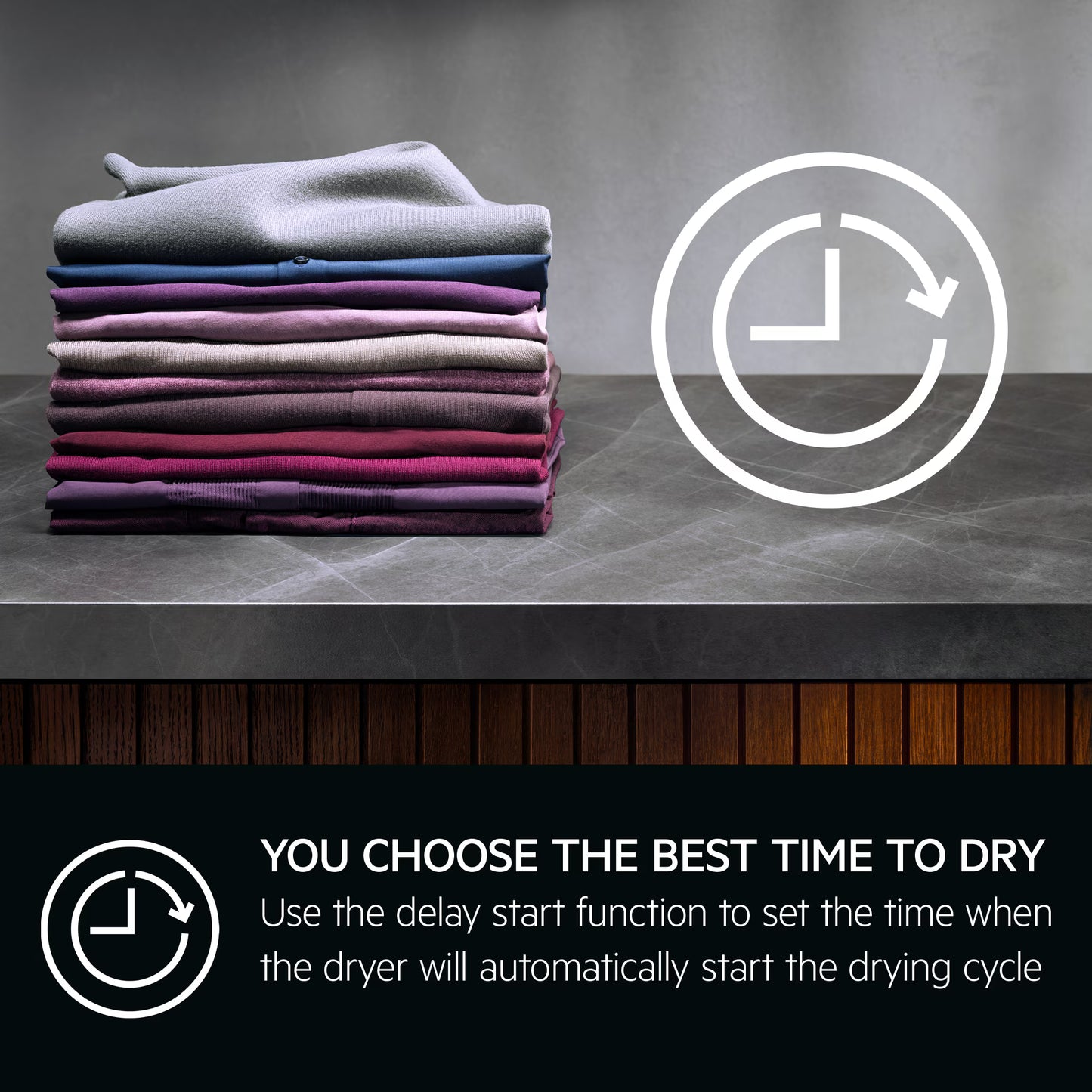 Stack of folded clothes on a gray surface with dryer symbol and text about AEG delay start function.