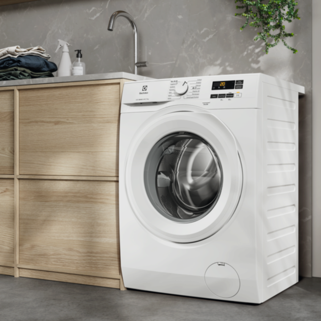 White Electrolux washing machine in a modern kitchen setting with wooden cabinets and a gray countertop.