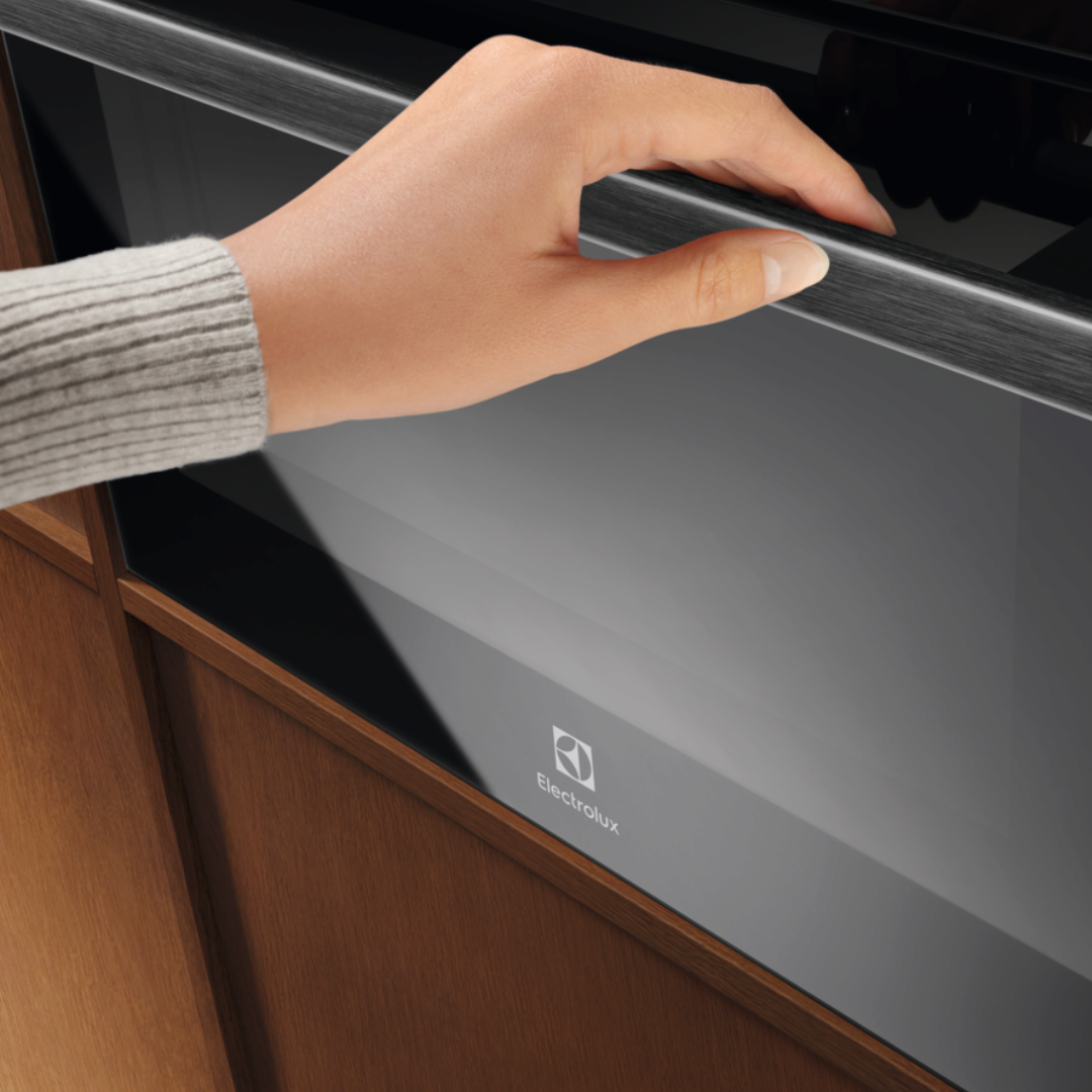 Hand opening a 600 Series CombiQuick® Microwave and Built-in Oven with wooden cabinet.