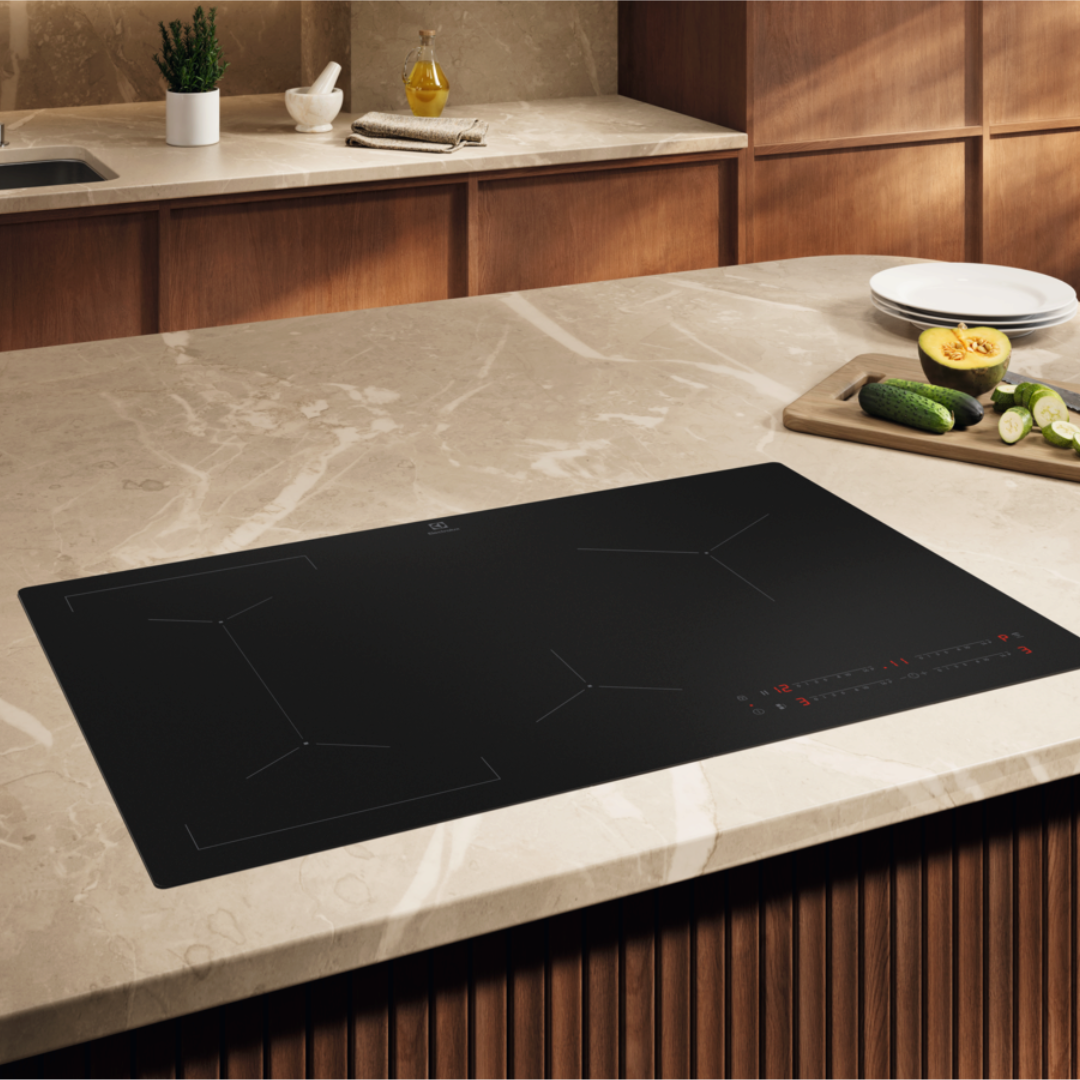 Black Electrolux induction hob on a kitchen countertop with wooden cabinets and a marble-like surface.