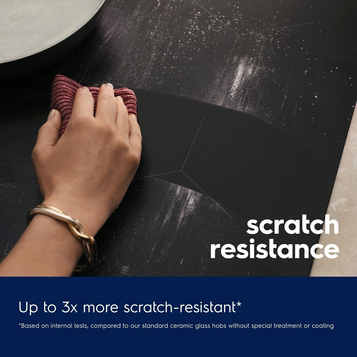 Hand using a purple scrubber on a Black Electrolux induction hob surface with text about scratch resistance.