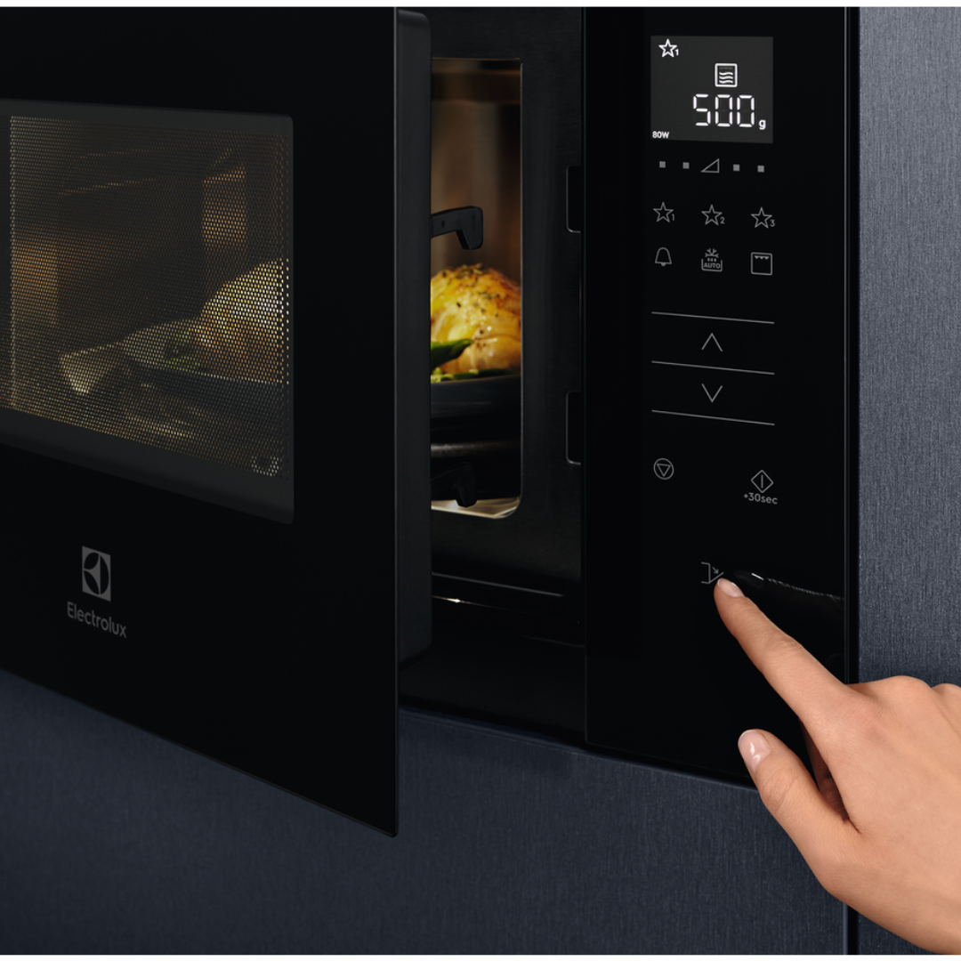 Black Electrolux microwave oven with a hand pressing a button on the control panel.