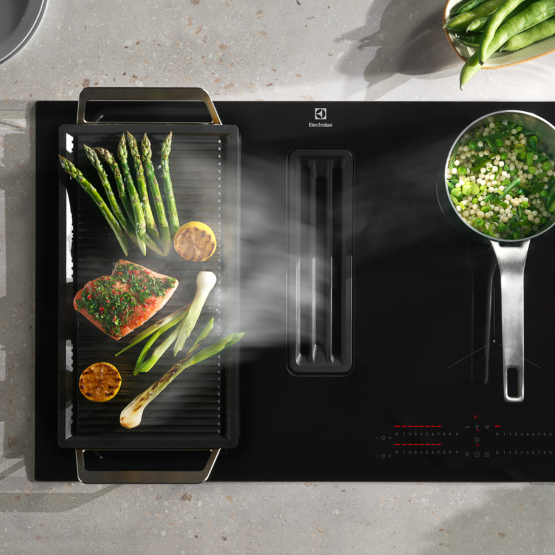 Electrolux Black Extraction induction Hobwith a grill pan, featuring food items like salmon and asparagus.