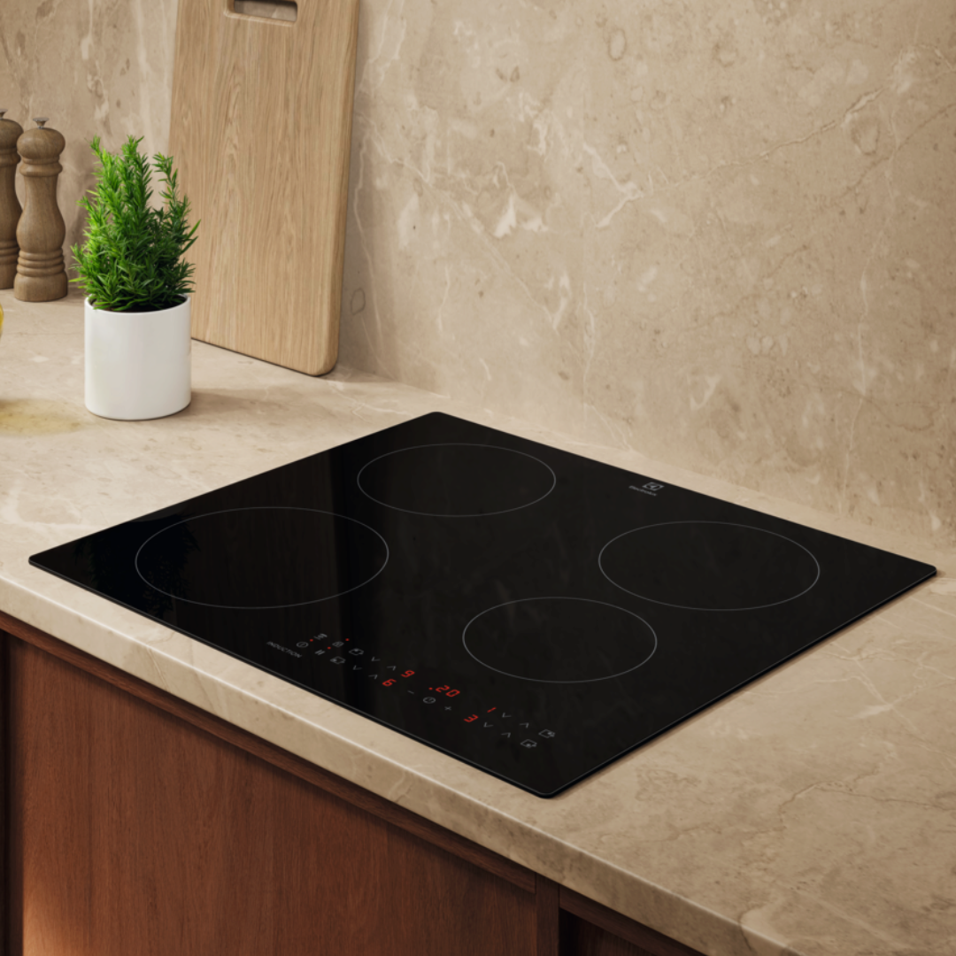 Black Electrolux Induction Hob on a kitchen countertop with a plant and cutting board in the background.