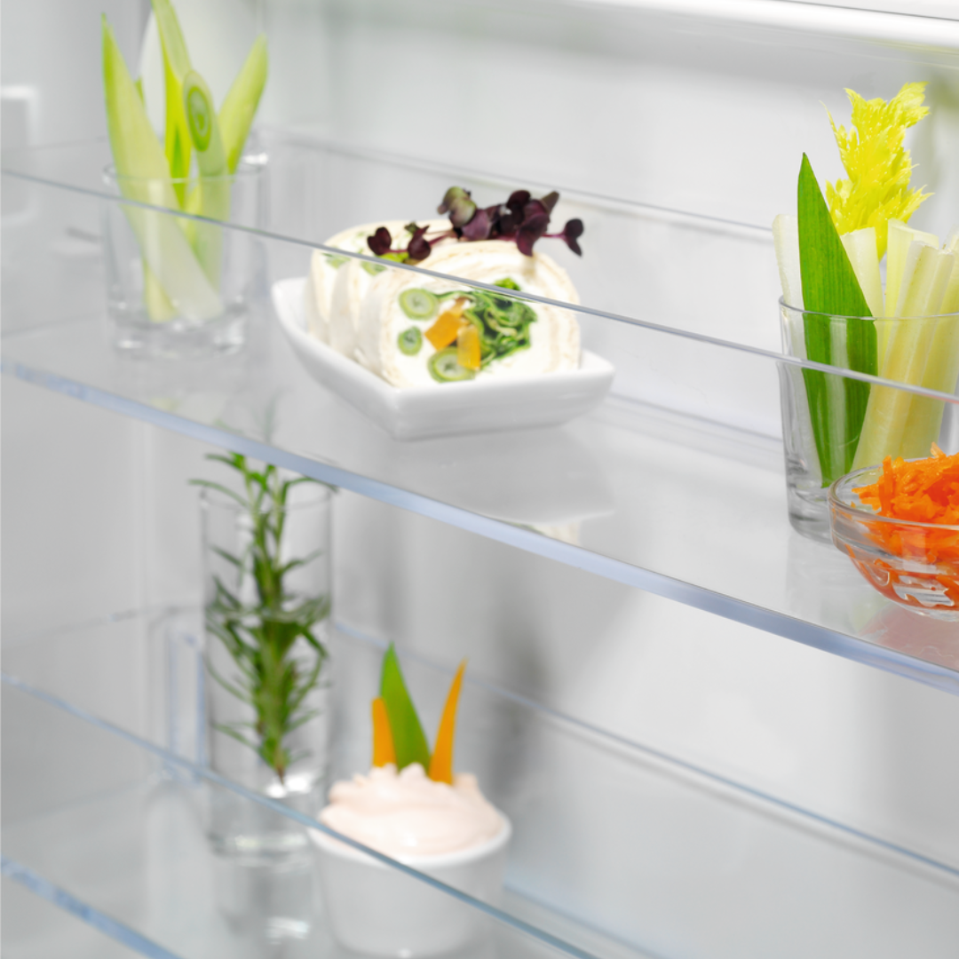 Clear glass shelves in an Electrolux Fridge with decorative items including a cake and plants.