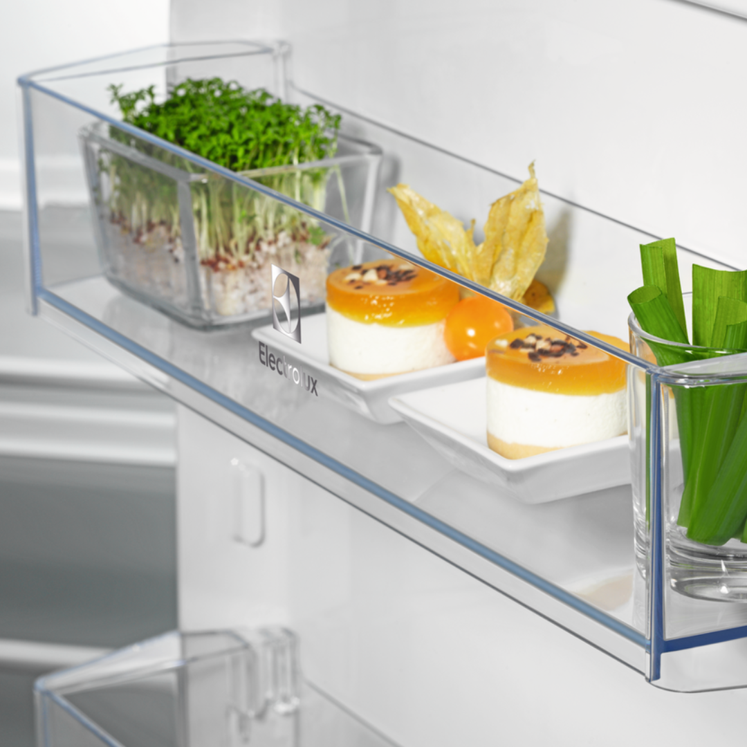 Clear Electrolux refrigerator drawer with food items including microgreens and fruits, branded 'Electrolux'.