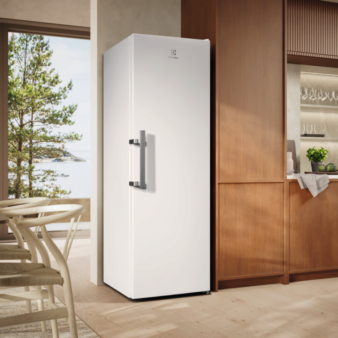 White Electrolux refrigerator in a modern kitchen with wooden cabinets and a view of trees and water.