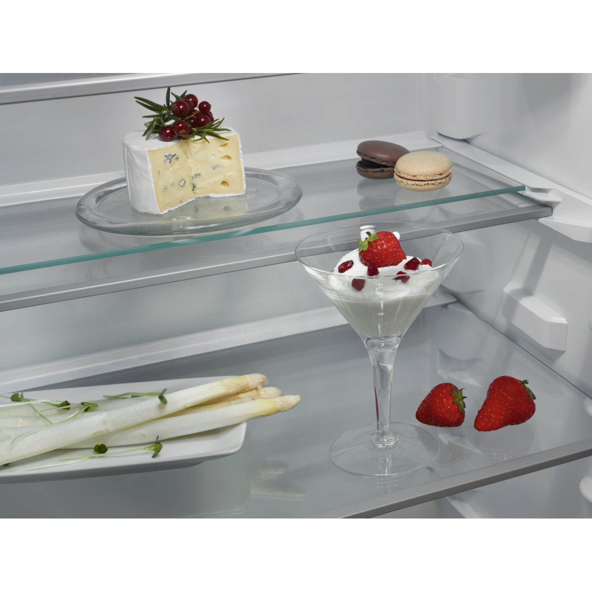 Open AEG refrigerator with glass shelves displaying food items like strawberries, asparagus, and a dessert.